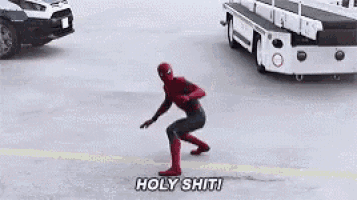 a man in a spiderman costume is standing in front of a police car and a truck .