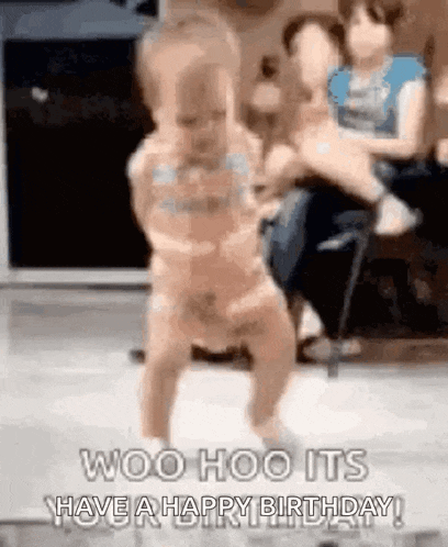 a baby is dancing in a room with a woman holding a baby in the background .