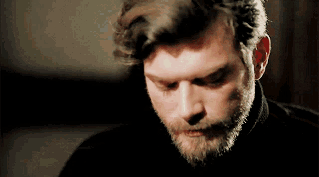a man with a beard wearing a black shirt looks down