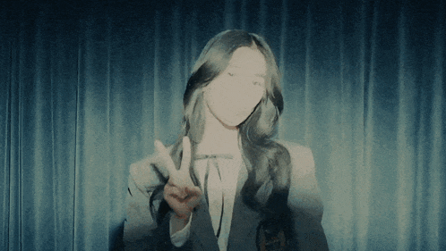 a woman giving a peace sign in front of a curtain