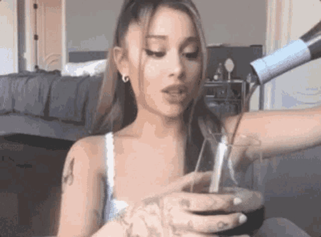 a woman is drinking from a glass with a straw while a hair dryer is blow drying her hair .