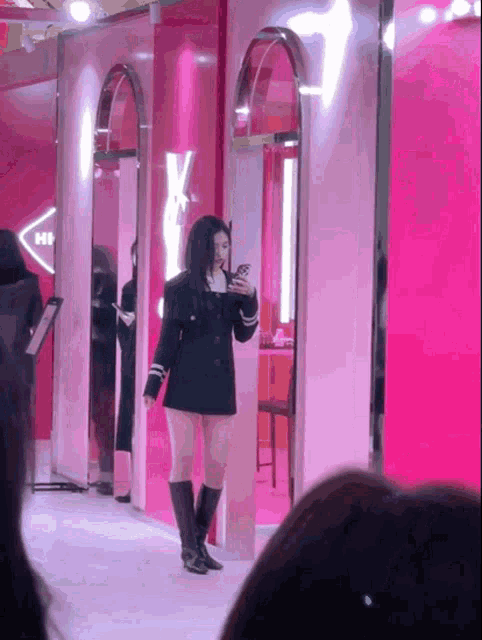 a woman taking a picture of herself in front of a pink wall with the letter x on it