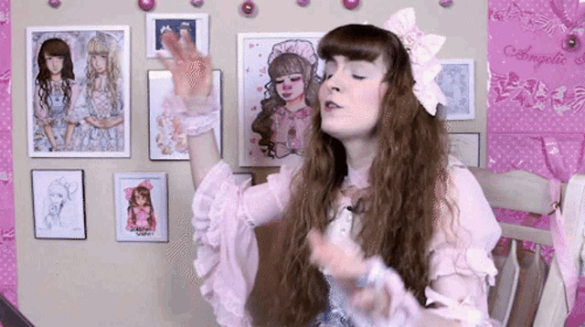 a girl in a pink dress is sitting in front of a wall with pictures on it