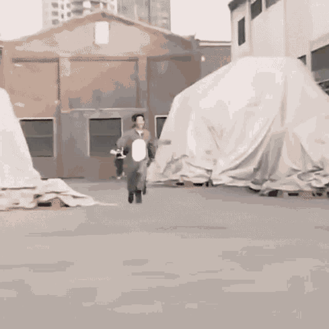 a man in a costume is running down a street in front of a large white tarp .
