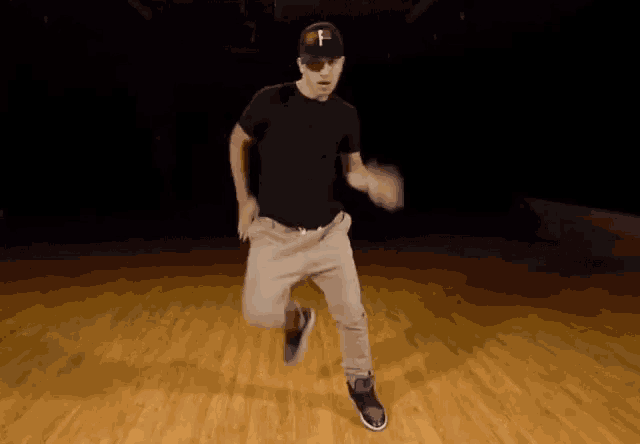 a man in a black shirt and gray pants is dancing on a wooden floor