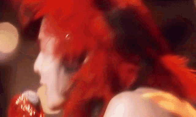 a close up of a person with red hair singing into a microphone
