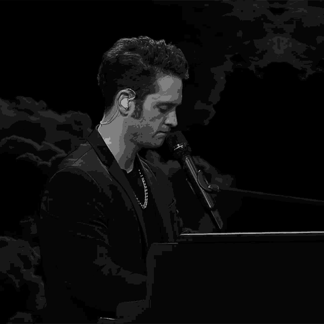 a man singing into a microphone while sitting at a piano