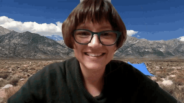 a woman wearing glasses and a black sweater smiles with mountains in the background
