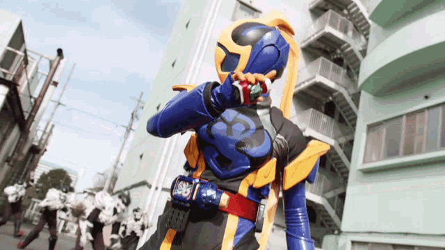 a man in a blue and yellow costume with the letter y on his chest is standing in front of a building