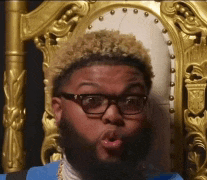 a man with glasses and a beard is sitting in a gold chair
