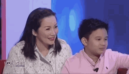 a woman and a boy are sitting next to each other on a television set .