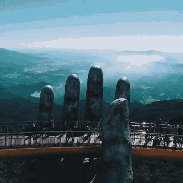a statue of a hand is on a bridge overlooking a valley