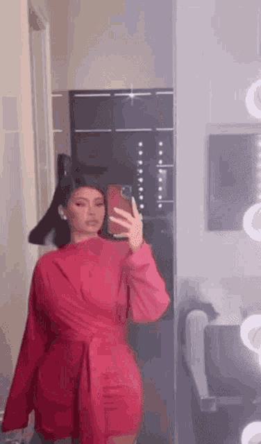 a woman in a red dress is taking a picture of herself in the mirror .