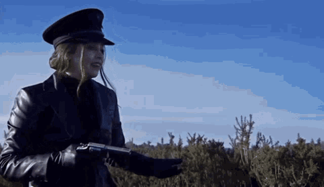 a woman in a hat and leather jacket is holding a gun in a field