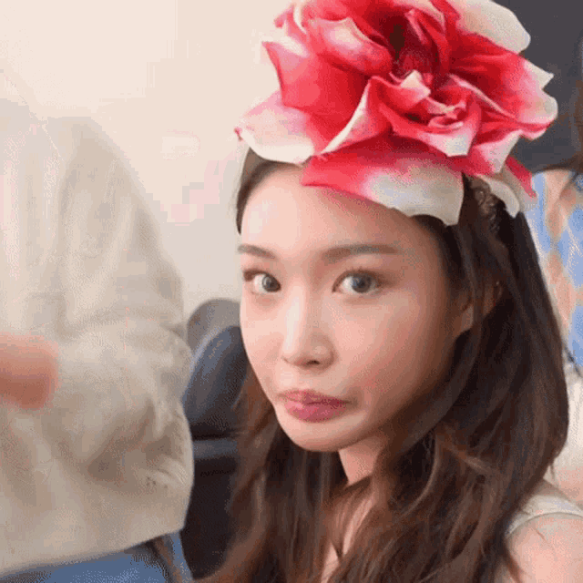 a woman wearing a red and white flower on her head making a face