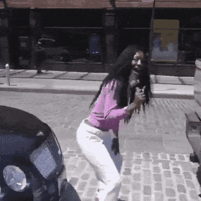 a woman in a pink shirt and white pants is standing on a sidewalk