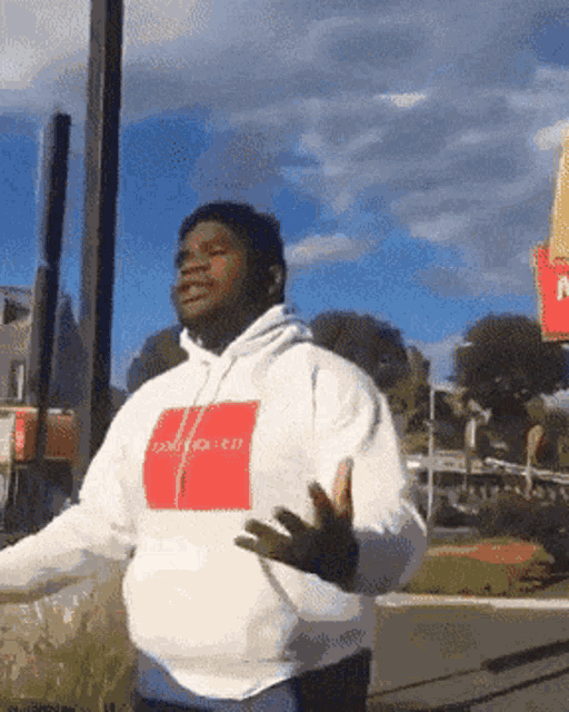 a man wearing a white hoodie with a red square on the front is dancing in front of a mcdonald 's