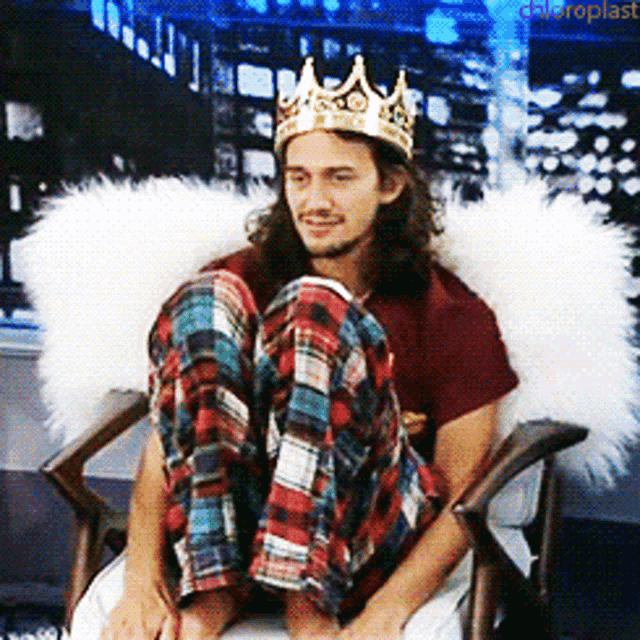 a man wearing a crown and plaid pants sits in a chair