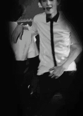 a black and white photo of a man in a white shirt and tie dancing on a stage .