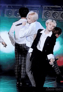 a group of men are dancing on a stage while one man holds a microphone .