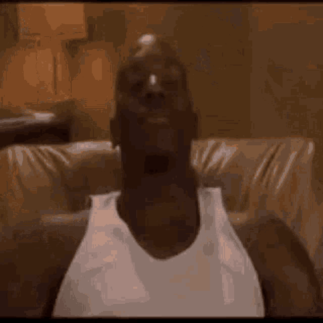 a man in a white tank top is laying on a couch .