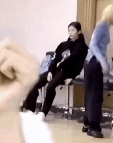 a woman is sitting on a chair in a room while another woman is standing behind her .