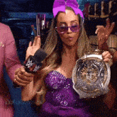 a woman in a purple dress is holding a trophy and a microphone