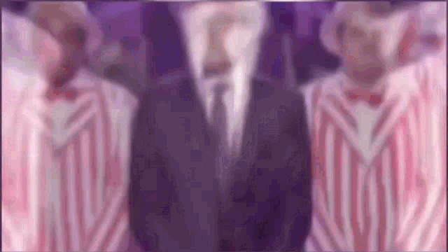 a man in a suit and tie is standing in front of two men in pink and white striped jackets .