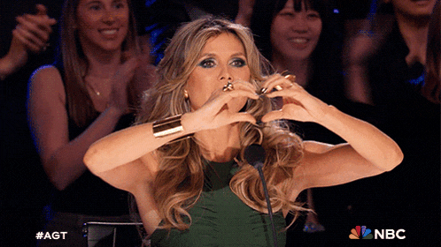 a woman in a green dress making a heart shape with her hands in front of a microphone