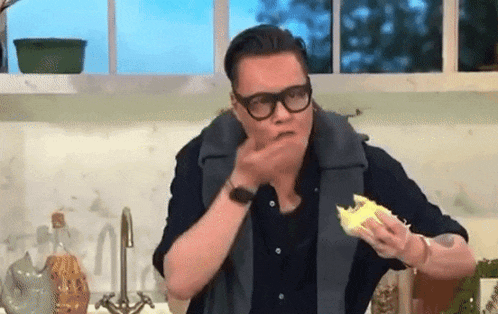 a man wearing glasses is eating a piece of food in a kitchen