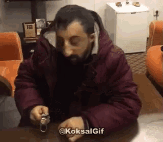 a man with a beard is sitting at a table looking at his watch