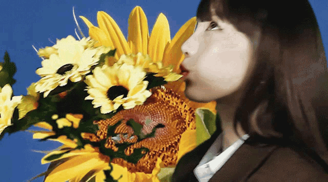 a woman blowing a kiss at a sunflower in front of a blue sky