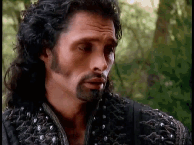 a man with long hair and a beard is wearing a black jacket with studs on the sleeves .