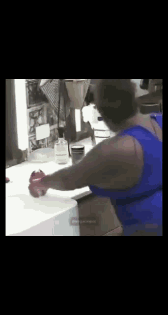 a woman in a blue tank top is holding an apple in front of a mirror