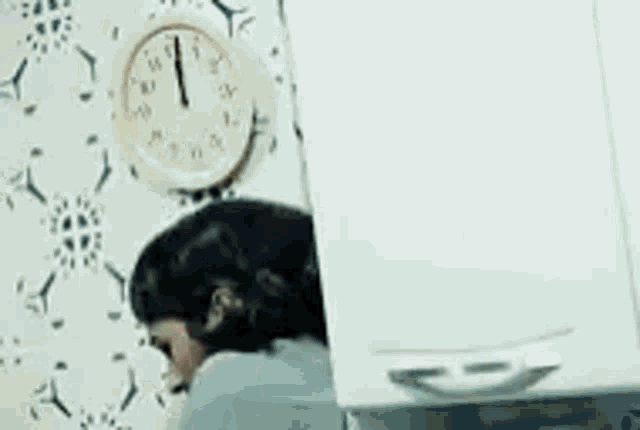 a woman is standing in front of a wall clock that shows the time as 11:55 .