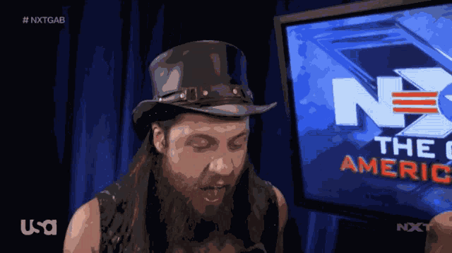 a man wearing a top hat stands in front of a screen that says nxt america