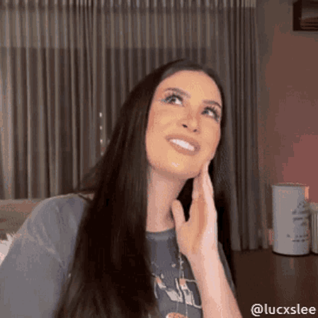 a woman with long hair is smiling and touching her face with her hand .