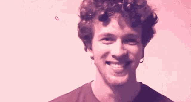 a young man with curly hair is smiling for the camera .