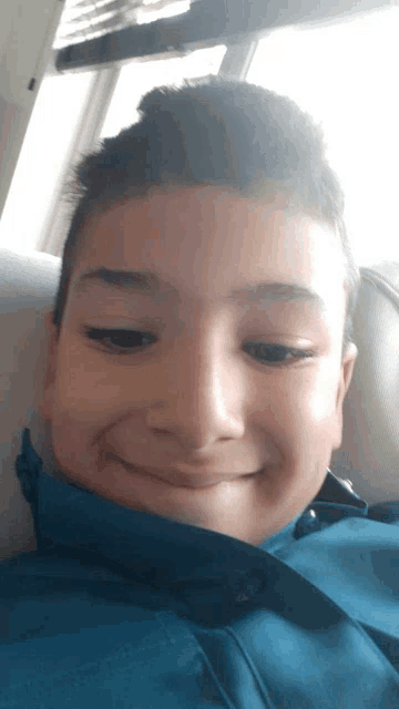 a young boy in a blue jacket is smiling for the camera while sitting on a couch .