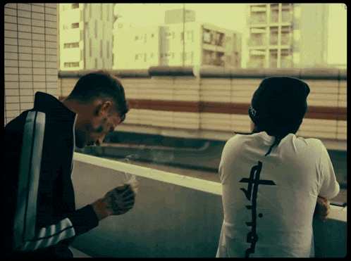 a man smoking a cigarette next to another man with a cross on his back