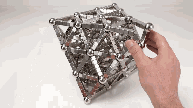 a hand is holding a cube made of magnetic balls