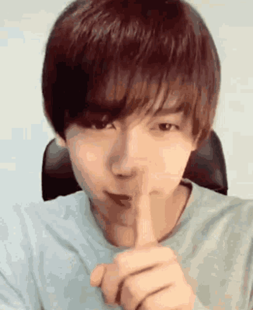 a young man is making a shhh sign with his finger .
