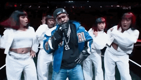 a man in a blue jacket is singing into a microphone while dancing with a group of dancers .