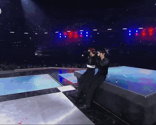 a man and a woman are sitting on a stage with a crowd watching