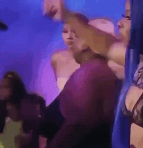 a group of people are dancing in a room with purple lights