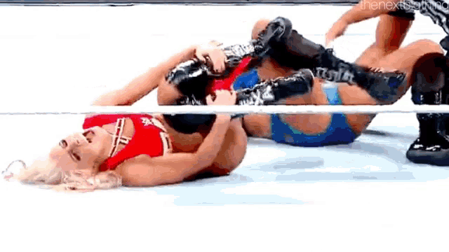 two women are wrestling in a wrestling ring and one is laying on the ground .