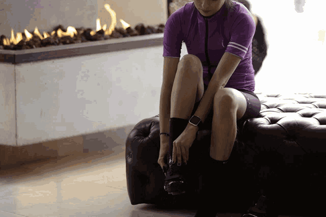 a woman in a purple shirt sits on an ottoman