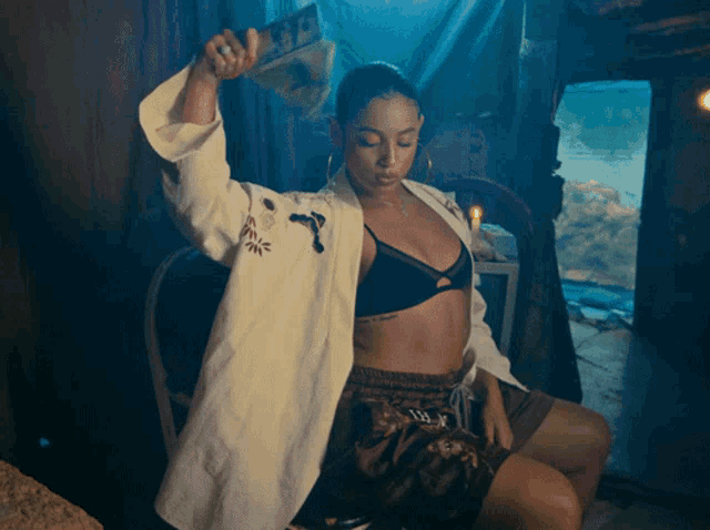 a woman in a bra and shorts is sitting in a chair holding a stack of money
