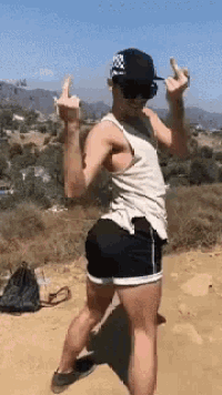 a man in a tank top and shorts is giving the middle finger while standing on a dirt road .