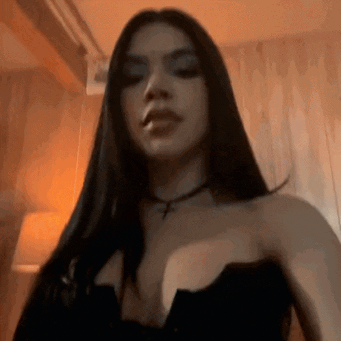 a woman with long black hair and a choker is standing in a room .